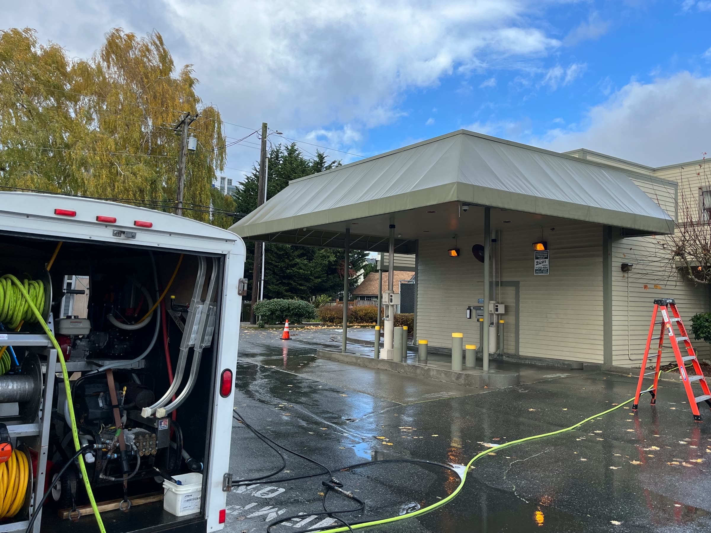 The same drive-through canopy washed clean over a wet parking lot, an orange ladder beside it.