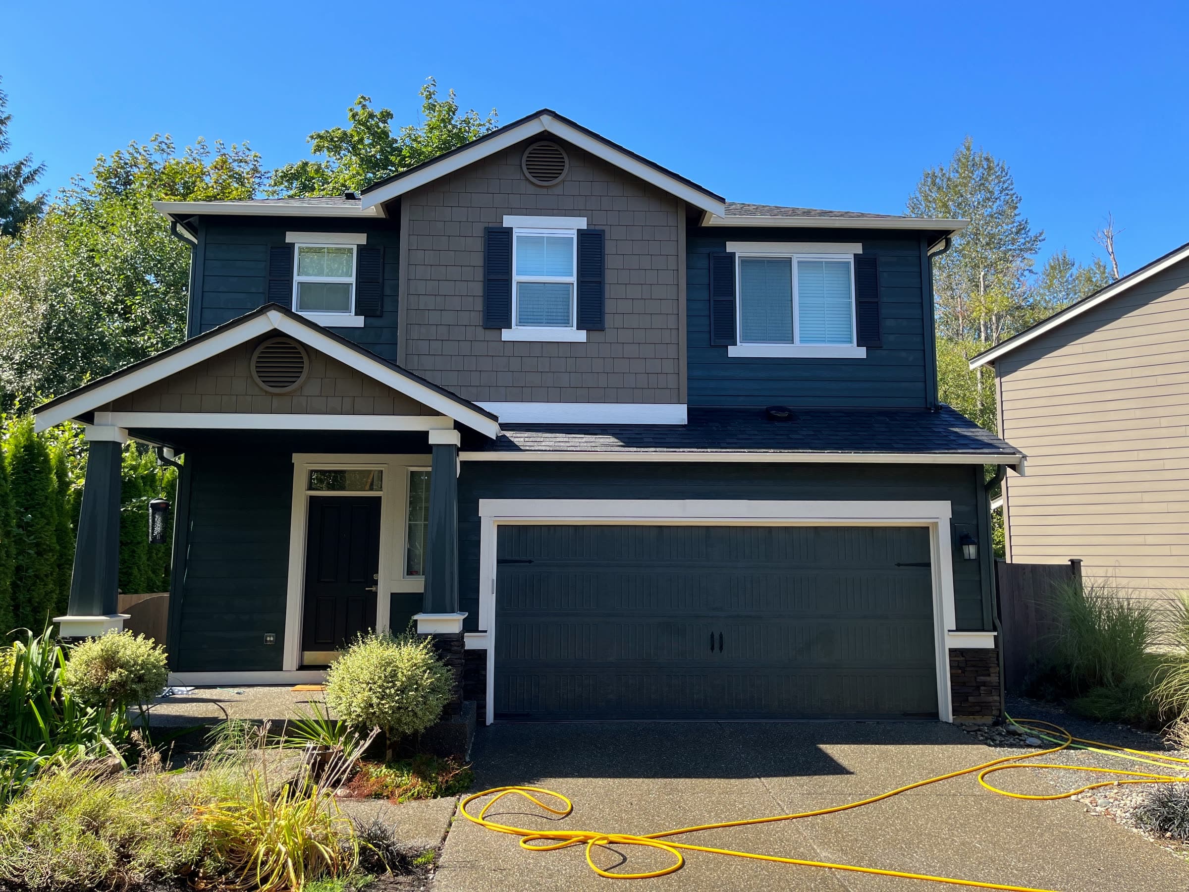 A navy two-storey house with white trim after a house wash, under a clear blue sky.