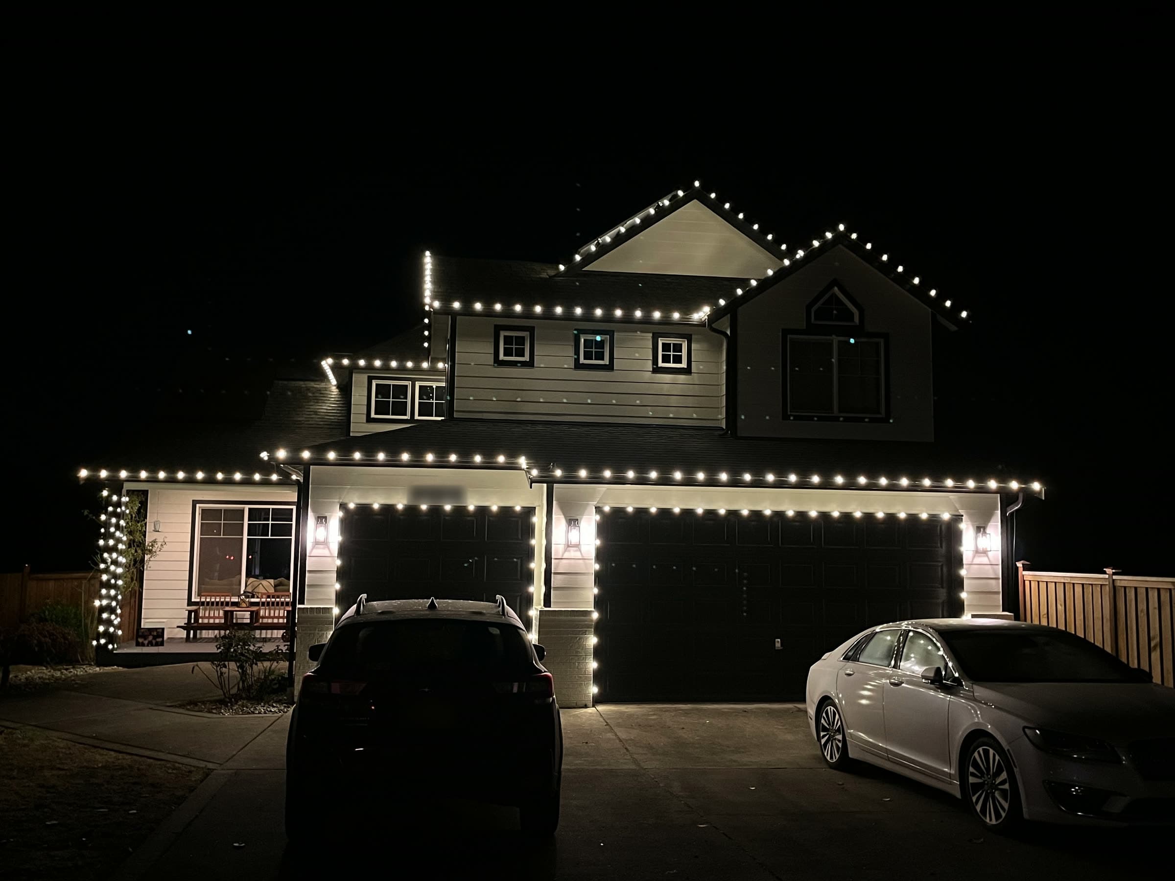 A two-storey house at night with white lights along every roofline and around the garage doors.