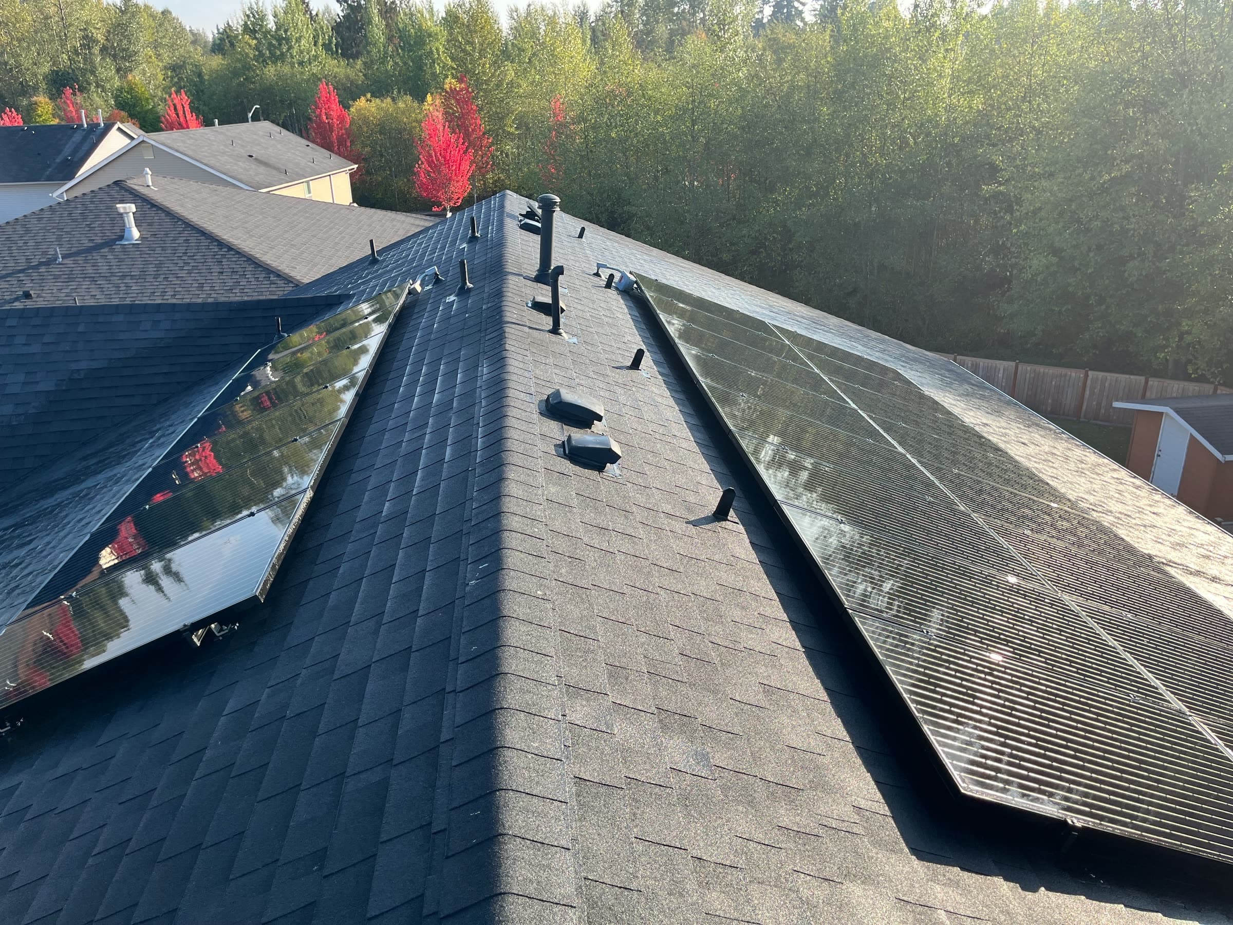 Clean solar panels on both sides of a roof ridge, bright red trees behind.