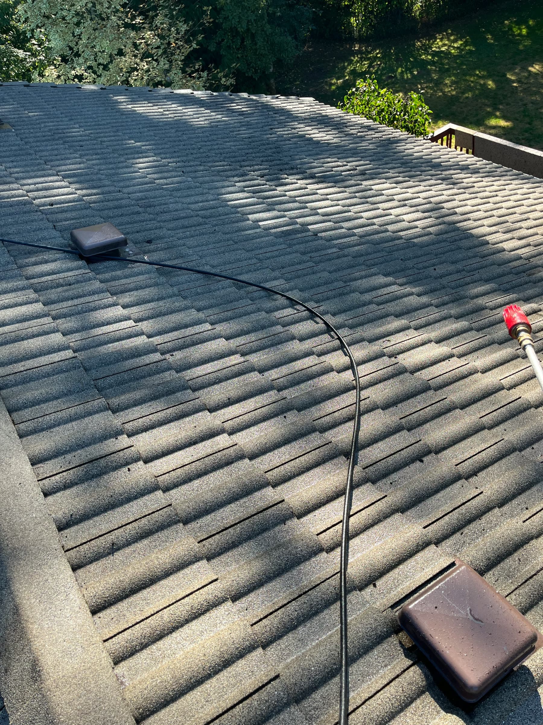 A clean, wet roof partway through a soft wash, the treatment hose running across it and the spray wand at the edge.